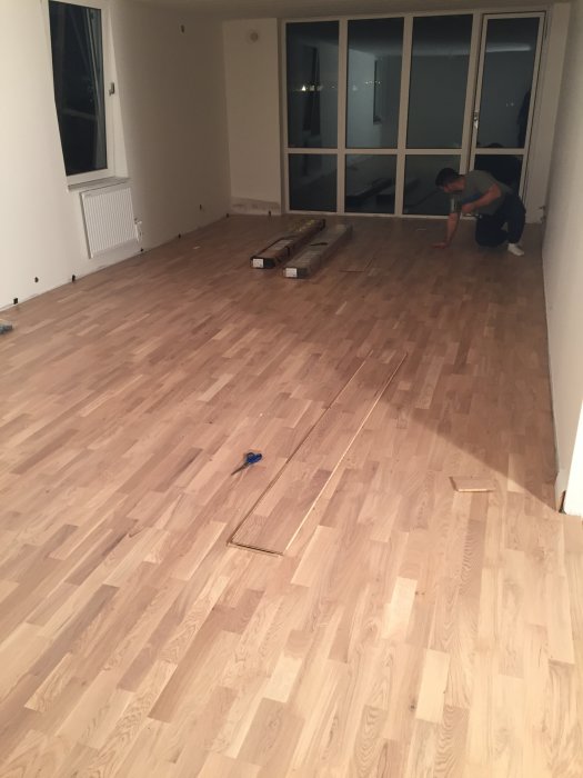 Person som lägger ett nytt trägolv i ett vardagsrum med verktyg på golvet