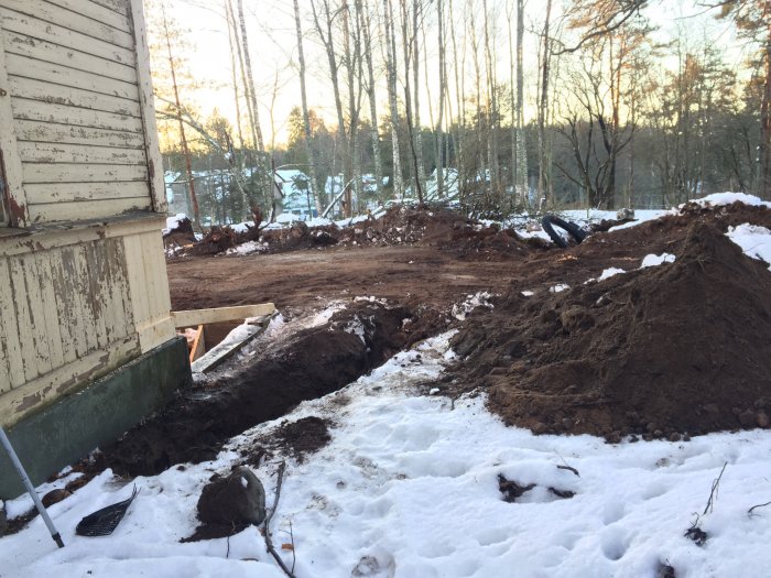 Grävd mark nära husvägg för installation av ny elkabel och kulvert med snö och jordhögar.