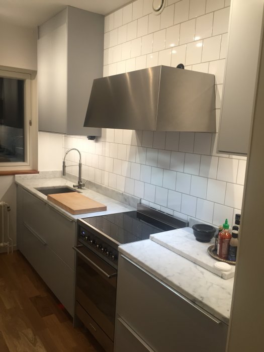 Modernt kök med IKEA stommar/fronter, vit marmorbänkskiva, SMEG spis och IKEA fläkt.