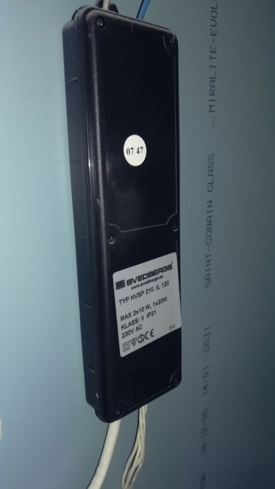 Svart transformator för spegelbelysning med specifikationsetikett, monterad på vägg.