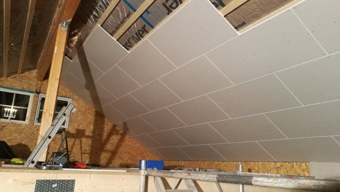 Renovering pågår i ett garage, gipstak under konstruktion med isolering synlig och stegar.