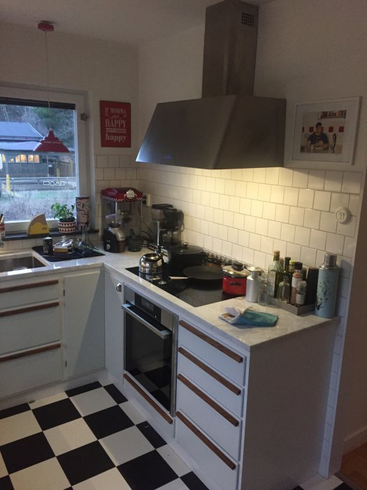 Köksfläkt monterad ovanför spisen i ett hemmakök med vita tegelväggar och svartvit rutigt golv.