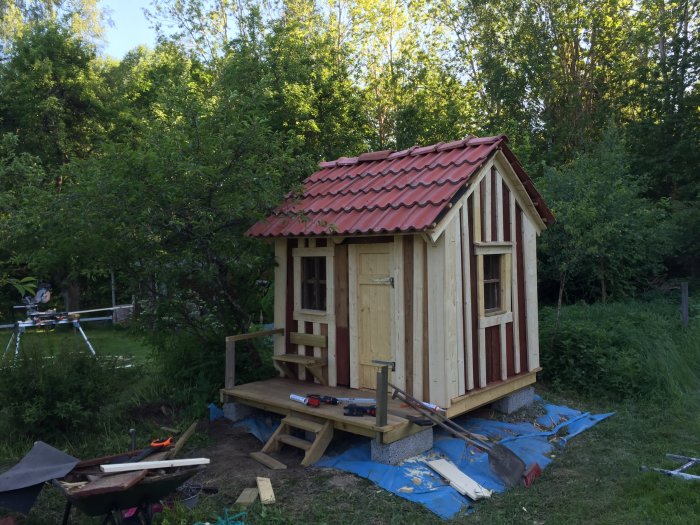 Nybyggt litet skjul med trästomme och röd takpannor mot en bakgrund av grönska.