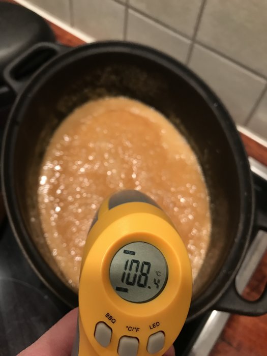 Termometer som visar 103.8 grader celsius över en kastrull med kokande knäck.