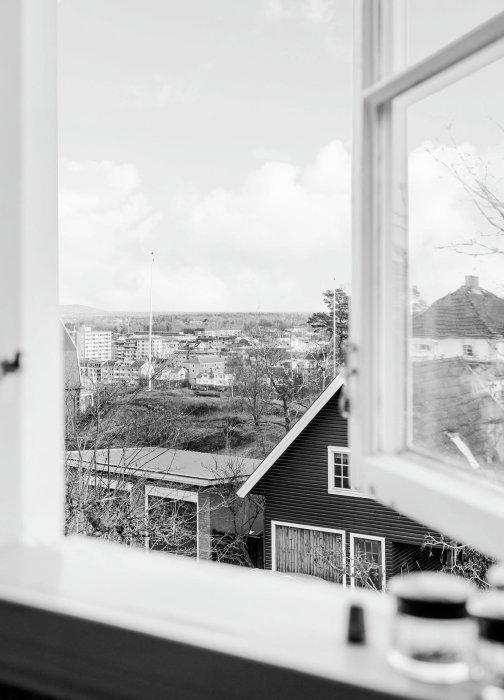 Svartvit bild av utsikt över Trollhättan från ett fönster, med träd och byggnader i förgrunden.