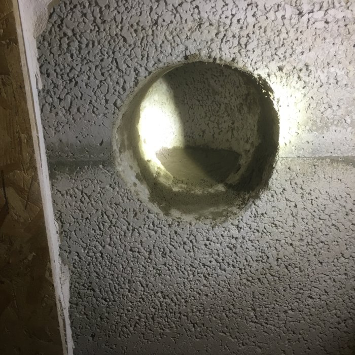 Öppning i en grå betongyta med singel och nygjuten topp synlig, eventuellt en del av ett byggprojekt.