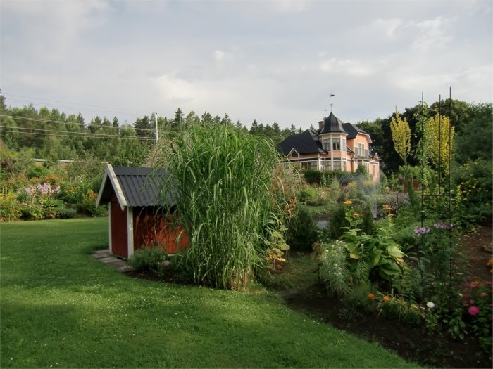 Välbevarat hus med torn och blomstrande trädgård med växthus och perenner.