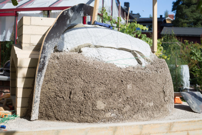 Lehmbackofen im Bau mit aufgetragener Lehm-Sand-Mischung und Metallschalung.