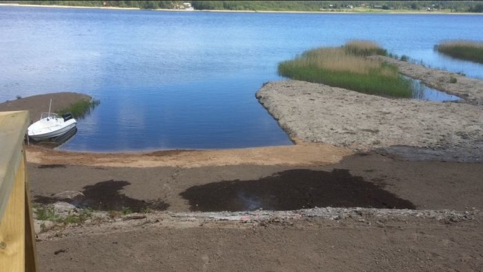 Renoveringsarbete vid en strand med en båt förtöjd nära en sandbank och vass, i klart vårväder.