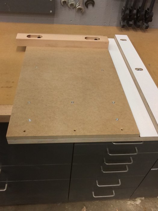 En hantverksbänk gjord av björkplywood med spår och anhåll i bok.