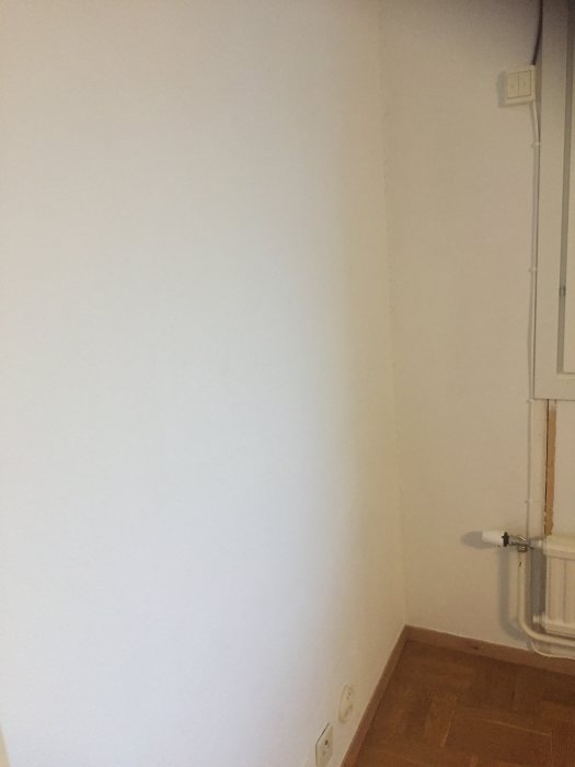 Vägg med strömbrytare, svart kabel som går ut genom väggen och vit kabel längs list under element.