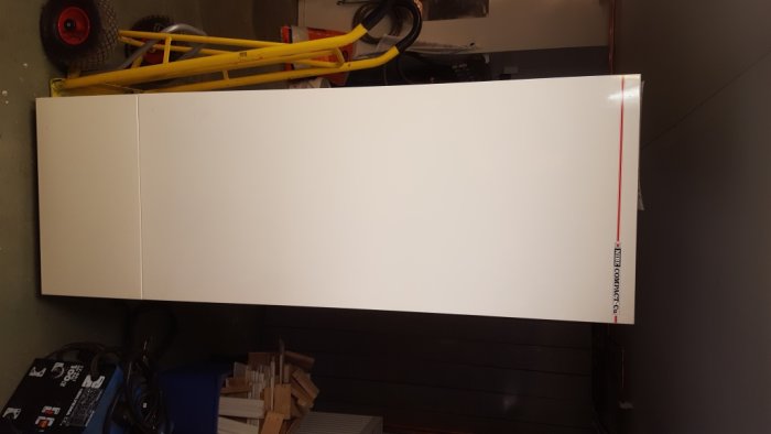 Lång vit skåpdörr upprätt på ett verkstadsgolv med byggmaterial i bakgrunden.