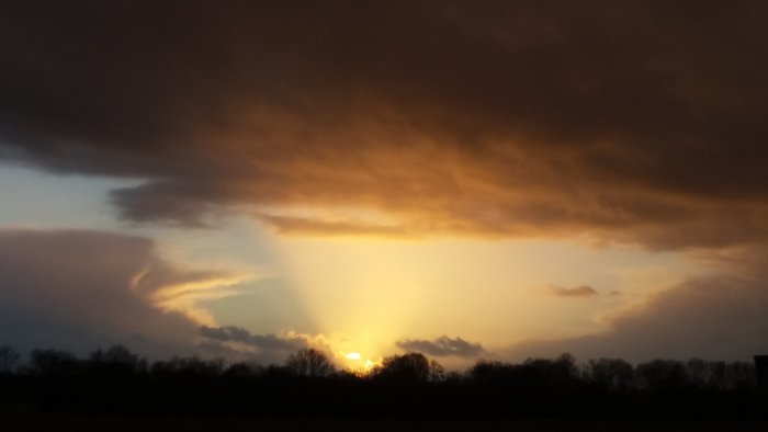 Dramatisk himmel med solnedgång och mörka moln som förebådar en storm.