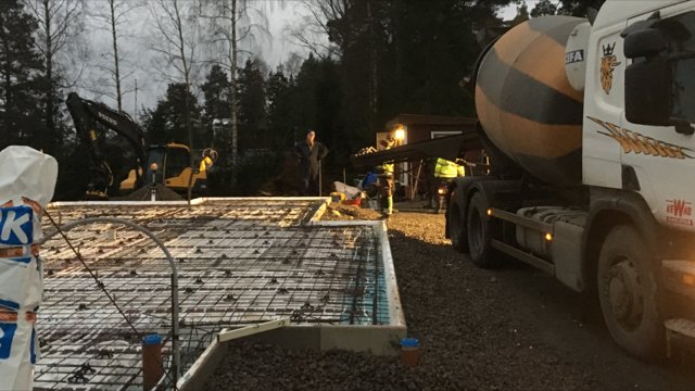 Gjutning av husgrund med armeringsjärn, betongbil och arbetare i arbete vid skymning.