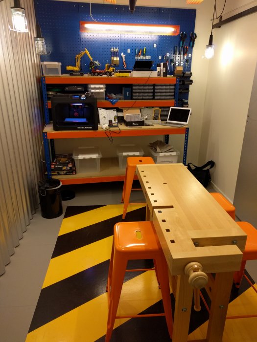 Ett välordnat hobbyrum med arbetsbänk, verktygstavla, belysning och 3D-skrivare.