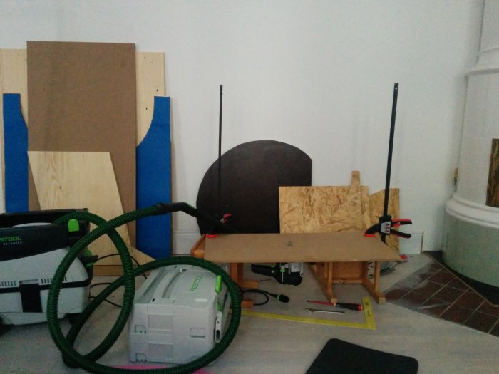 Improviserad fräsanordning med MDF-skiva fastspänd på barnstolar i ett vardagsrum.