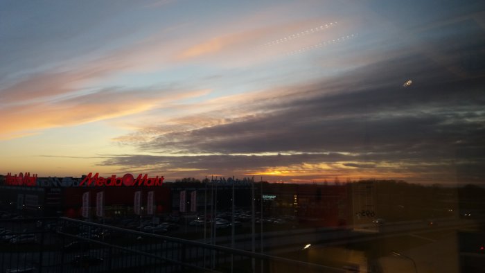 Solnedgång med färgsprakande himmel över varuhusparkering sedd genom fönster.