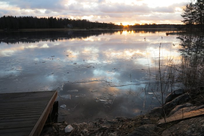 Soluppgången reflekteras i en isbelagd sjö sedd från en brygga, symboliserande platsen för premiärbad efter bastu.