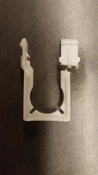 Uppskuren vit plastklämma med synliga brottytor på en grå yta, svår att demontera utan skador.