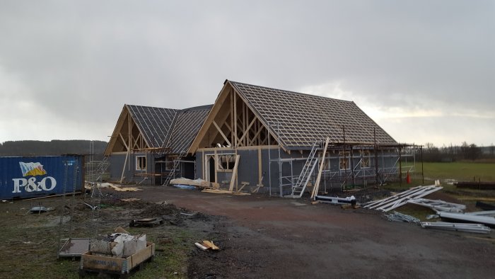 Halvbyggt hus med takstomme som stått emot en storm, omgivet av byggnadsställningar och material.