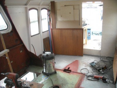 Renoveringsarbete på en båts övre däck med verktyg utspridda, avsågat däckshus och nytt skott under konstruktion.