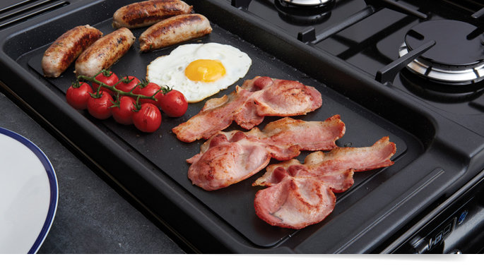 Stekbord med bacon, korv, ägg och tomat på gas- eller induktionshäll.