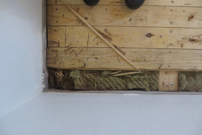 Skadad del av ett källargolv med lossnade träbrädor och synlig isolering under.