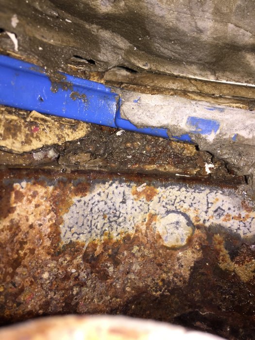 Del av rostigt bjälklag i gammal byggnad med synliga rör och betongfragment.