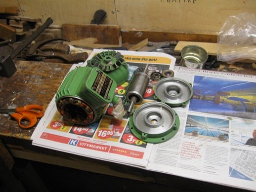 Demonterad motor och lagerhus med nya lager för renovering på ett arbetsbord med verktyg och tidningar.