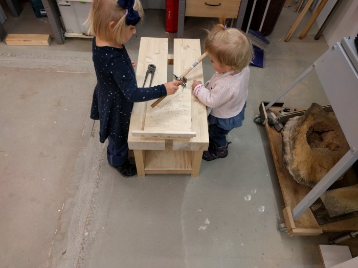 Två små barn hjälper till med snickeri i en verkstad.