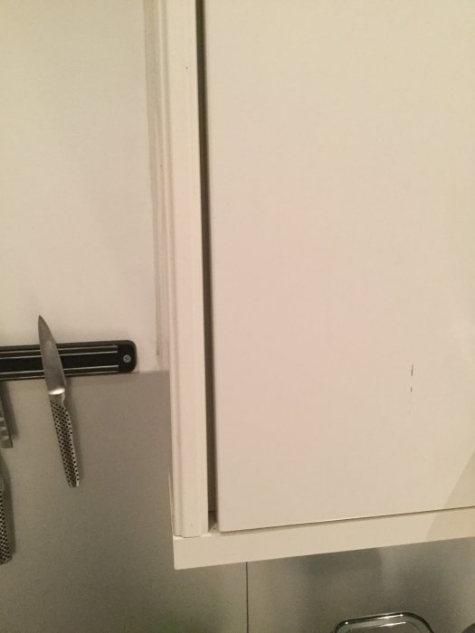 Detaljbild på vit kökslucka med profilerad kant och handtag, samt infästning nära en knivmagnet.