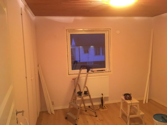 Tomt barnsovsrum före renovering med trägolv och fönster, trappstege och renoveringsmaterial synliga.