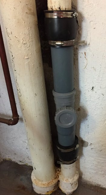 Reparerat gjutjärnsrör med klämmuff och nya PVC-sektioner i en källare.