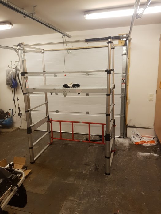 Nymonterad metallställning i ett garage, troligen en Zip-up kopia, med tom kartong och byggmaterial på golvet.