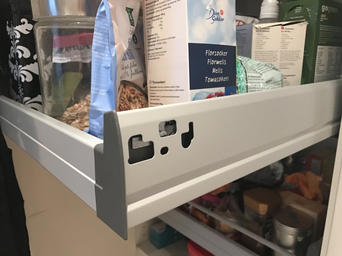 Öppen kökslåda med matförpackningar och saknade skruvbrickor i handtagets fästpunkter.