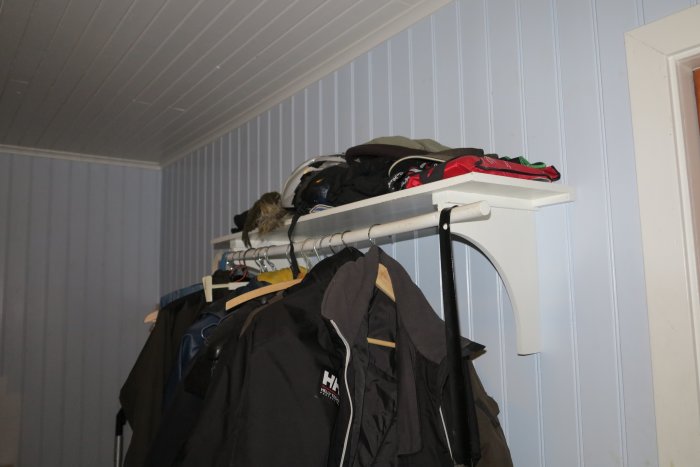 Hylla tillverkad av engångspall med kvastskaft används som klädhängare och förvaring.