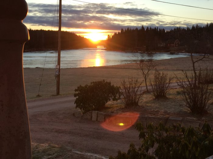 Soluppgång över en frusen Västerdalälven med träd och hus i silhuett mot morgonhimlen.