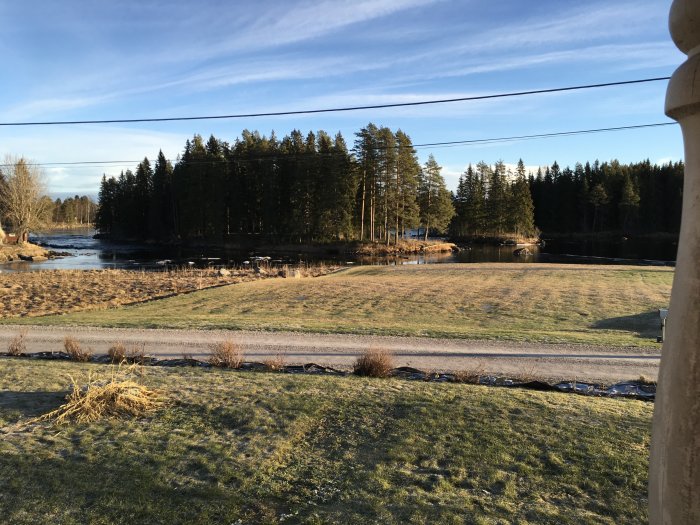Utsikt över en flod med frodiga träd och en grävd stig, med en stolpe i förgrunden till vänster.
