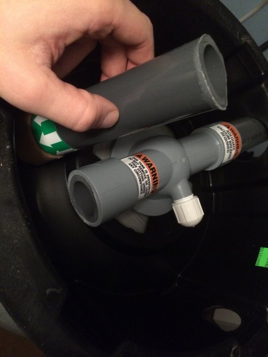 Hand håller en skadad hydrofor-del med synliga sprickor och varningsetiketter.