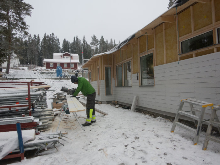 Person som spikar träpanel på ett hus under konstruktion i vinterscen.