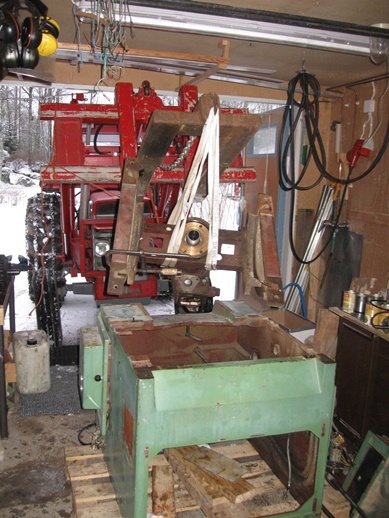 Demontering av maskindelar med en röd Massey-Ferguson 165 traktor och frontlastare i ett garage, med en grön del på en pall framför.