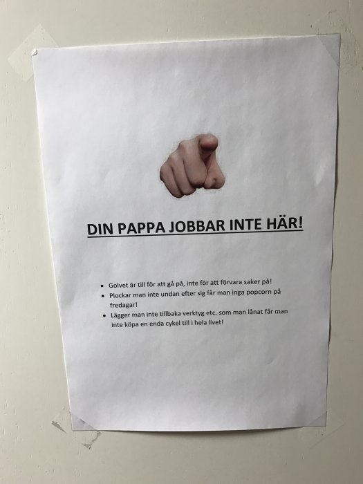 Vit anslagstavla med pekande finger och text "DIN PAPPA JOBBAR INTE HÄR!" samt listade förhållningsregler på vägg.