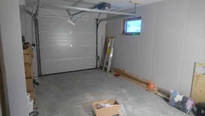 Nyinstallerad garageport i en halvfärdig garageinteriör med byggmaterial och verktyg utspridda.