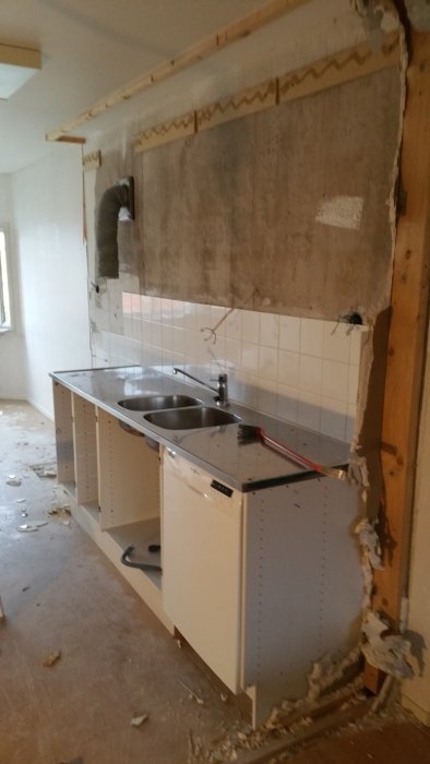 Kök under renovering med borttaget överskåp och synliga väggskador.