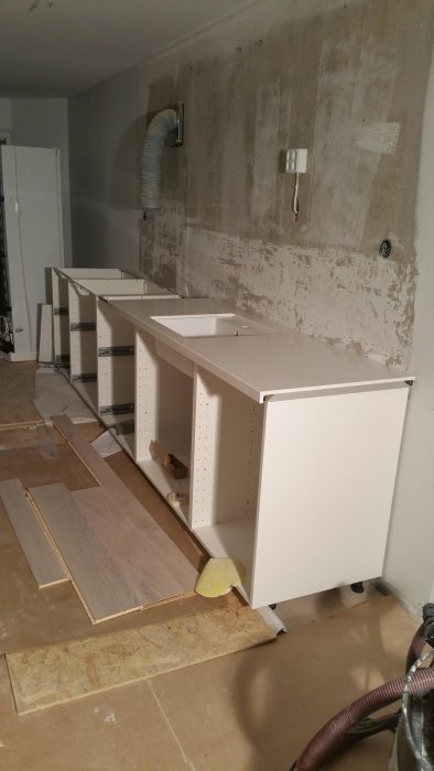 Renovering av kök, ofärdiga skåp, osätta kakelplattor, exponerade vägguttag, rörstam, rå vägg, byggmaterial, arbetsbelysning.