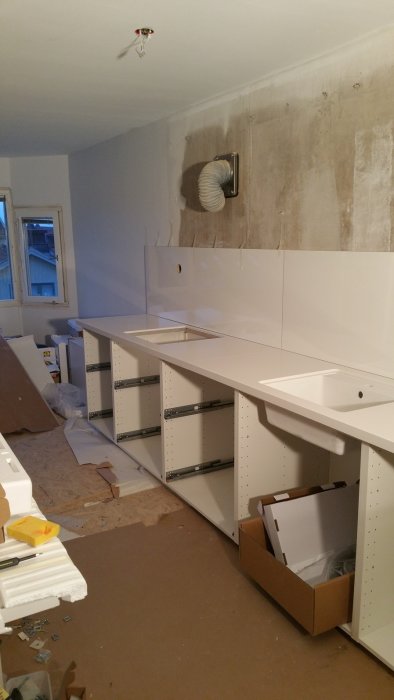 Köksrenovering med oskåpade vita skåpstommar och arbetsbänk, väggen ovanför är ännu obehandlad.