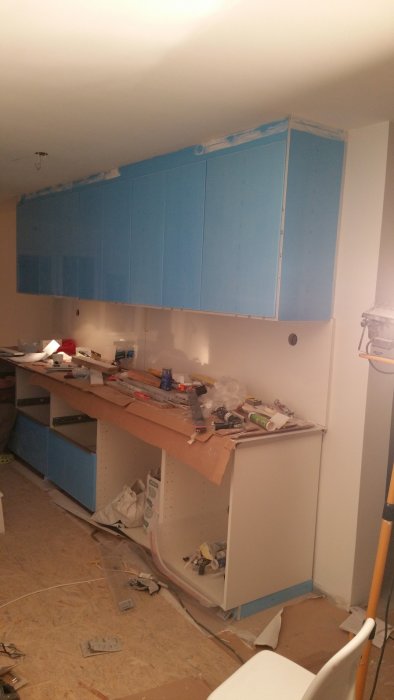 Pågående köksrenovering med blå skåpluckor och verktyg utspridda på en diskbänk.