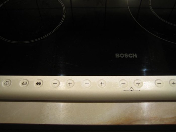 Översikt på en BOSCH-spishäll med vit kontrollpanel och symboler för funktioner och inställningar.