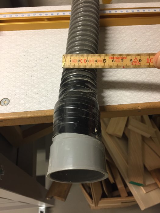 Flexibel Bauhaus-slang med tumstock för mätning mot en bakgrund av träbitar.