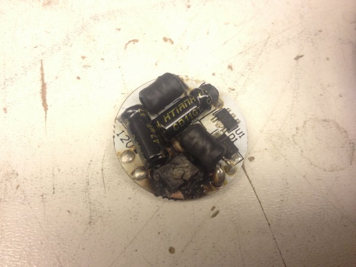 Skadad LED-drivare med tecken på överhettning och smälta komponenter på en vit bakgrund.